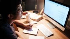 A male student studying in the evening light at his desk.